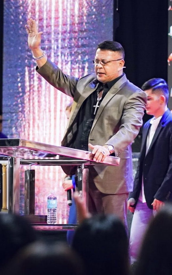 Bishop Rod Cubos with his hand raised in prayer at the pulpit during a Christ the Healer worship service in Davao City