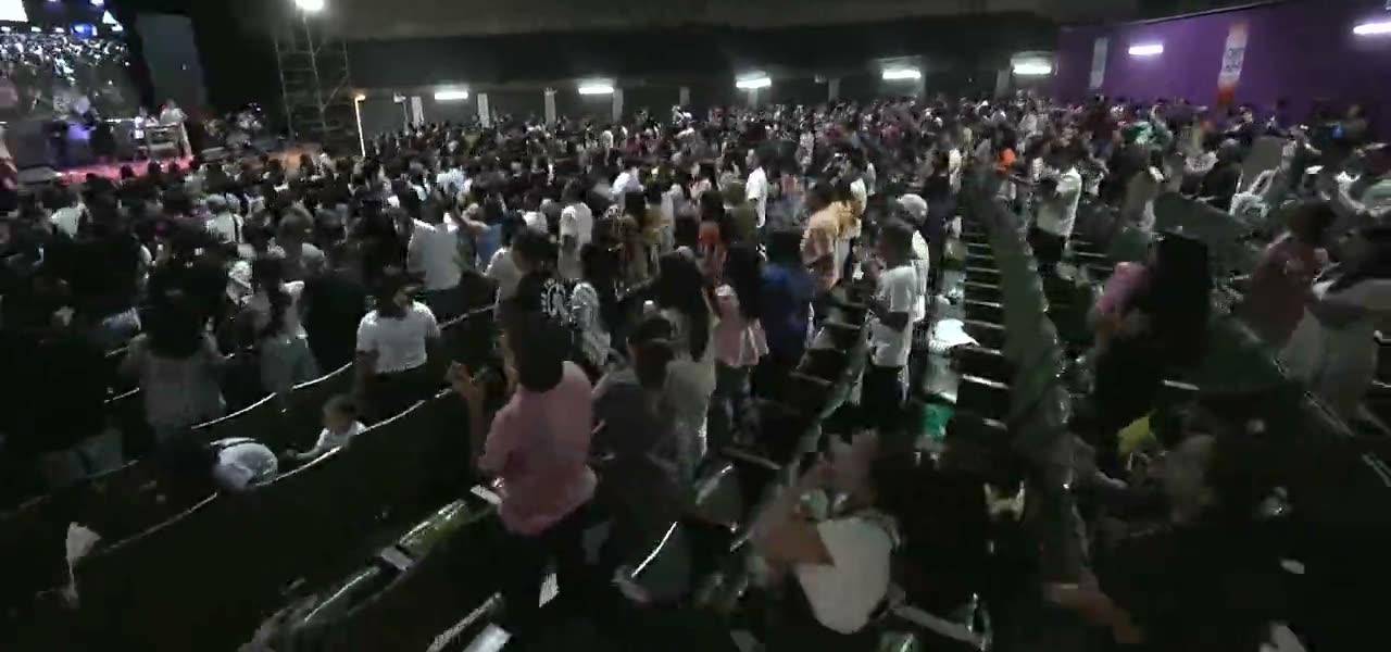 A packed arena of people standing with hands raised in worship